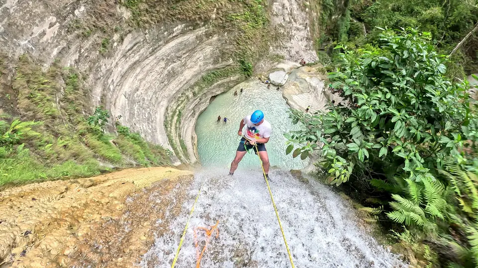 Guest rappelling down a waterfall toward the round turquoise pool at Dao Falls