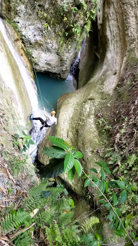 Looking down on a guest rappelling beside a waterfall into a deep teal pool