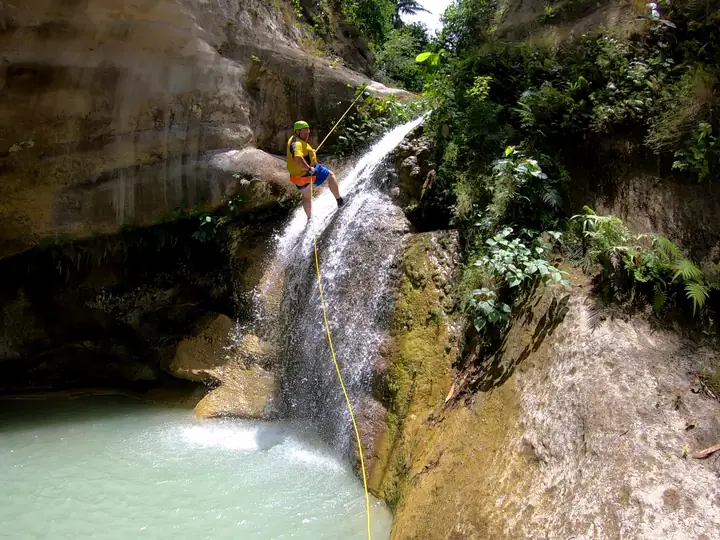 Guest rappelling down a waterfall into a turquoise pool